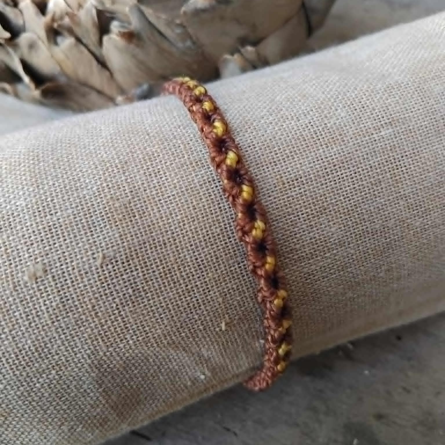 A handcrafted macrame bracelet in brown and yellow waxed cord.