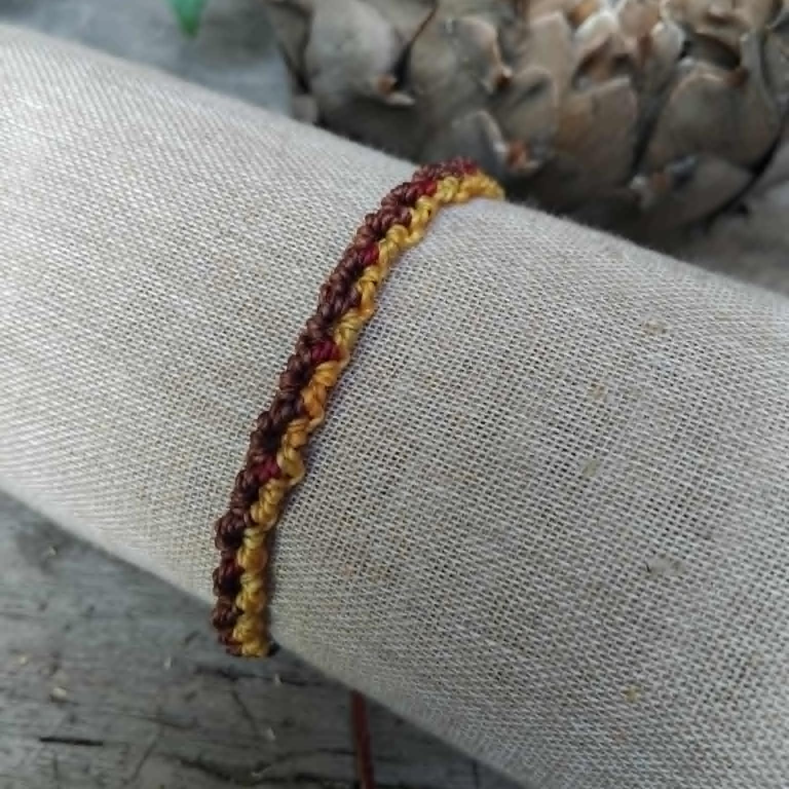 Handcrafted Macrame Knotted bracelet in chocolate brown, saffron yellow and burgundy red cord.  Displayed on a beige linen sleeve.