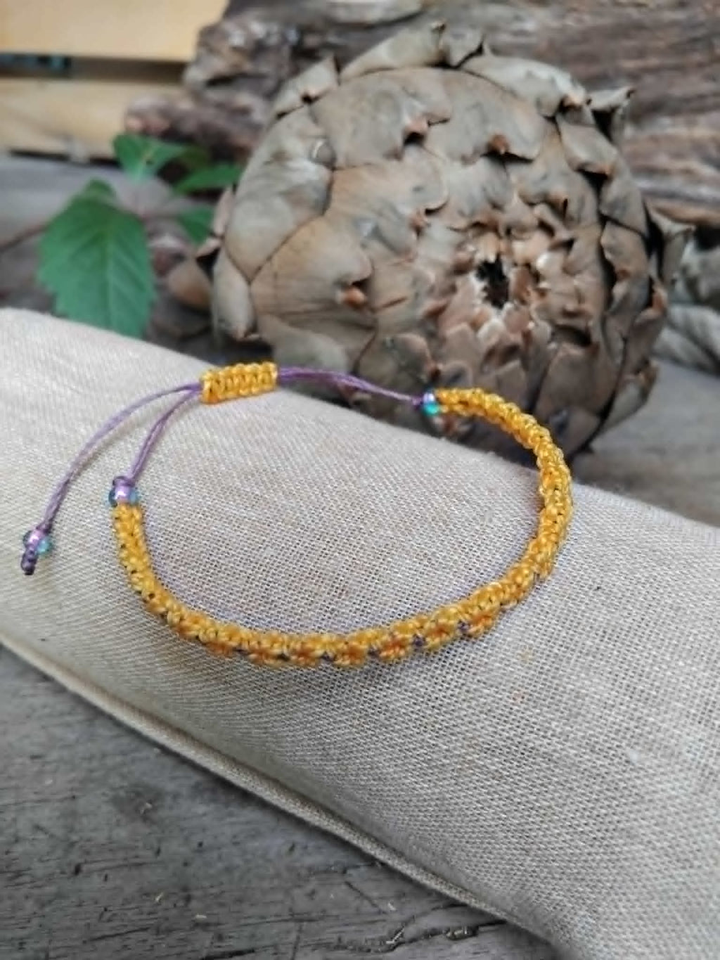 Handcrafted macrame bracelet in saffron yellow and lavender waxed cord.  Displayed on a beige linen sleeve with rustic background.
