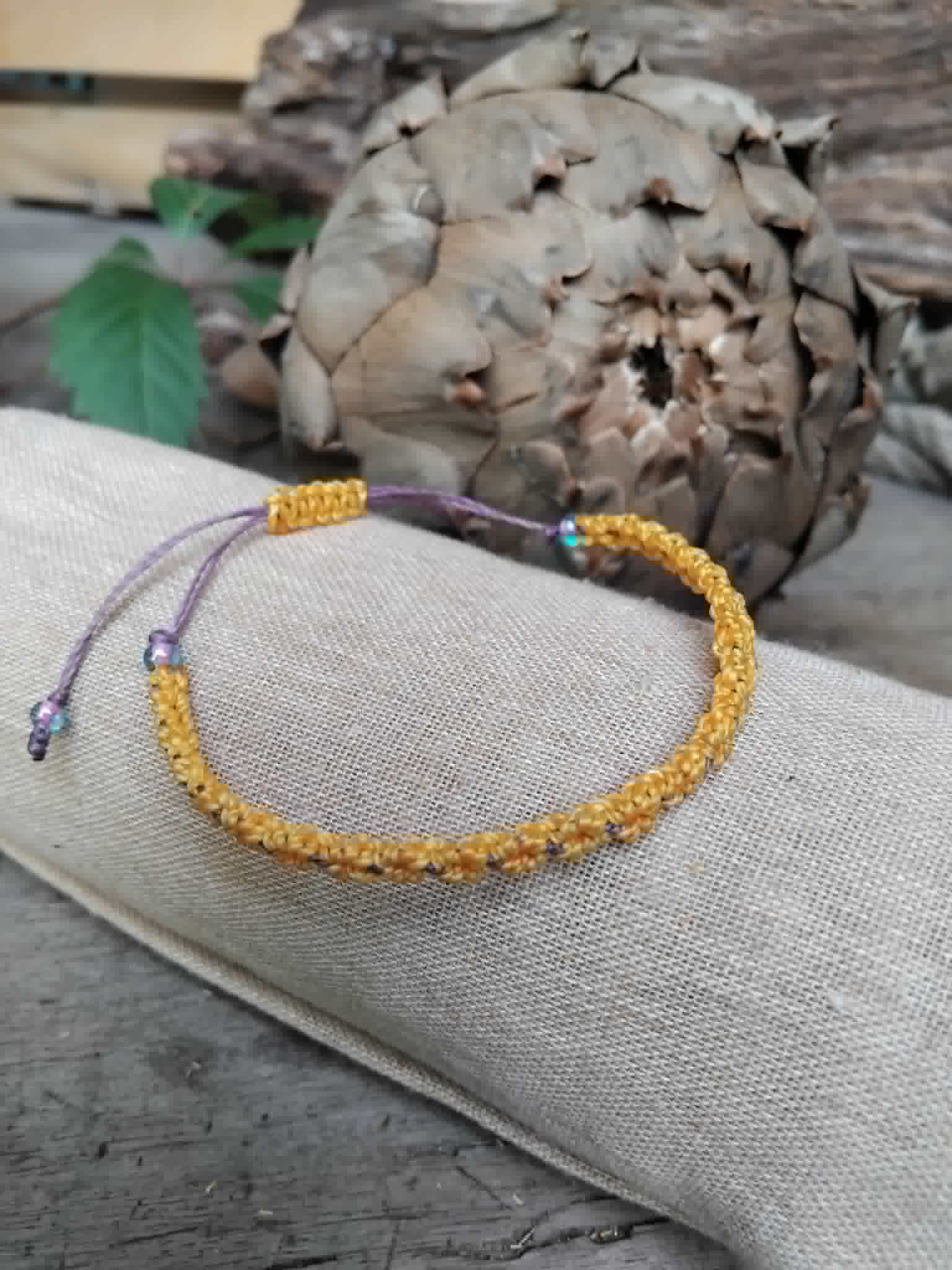 Handcrafted macrame bracelet in saffron yellow and lavender waxed cord.  Displayed on a beige linen sleeve with rustic background.