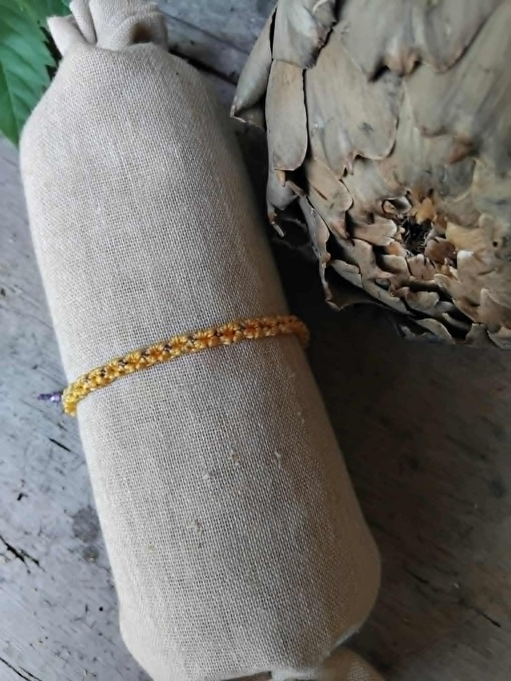 Handcrafted macrame bracelet in saffron yellow and lavender waxed cord.  Displayed on a beige linen sleeve with rustic background.