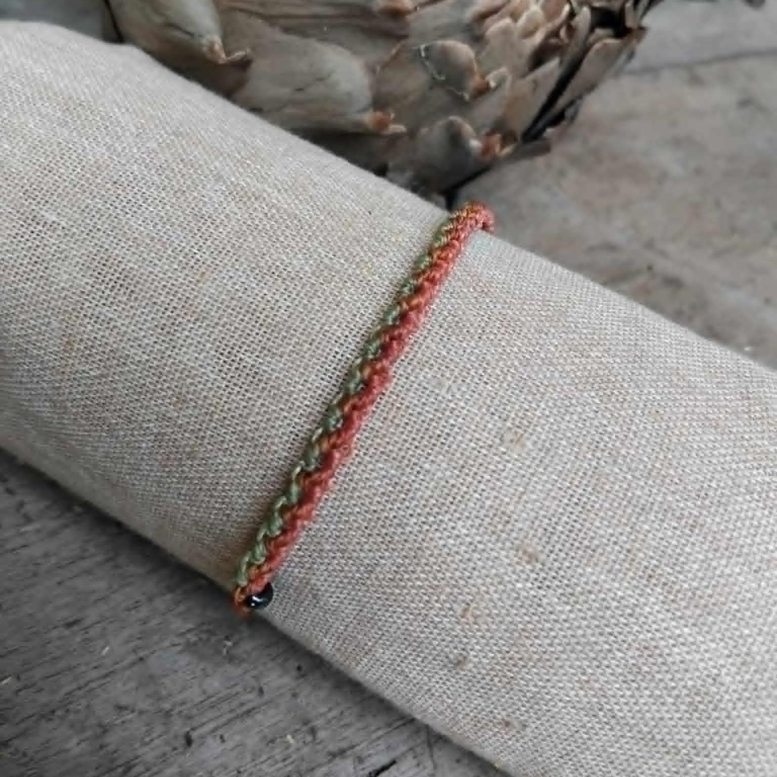 Slim Macrame Bracelet in coral and pale lime green toned waxed cord.  Displayed on a beige linen sleeve.
