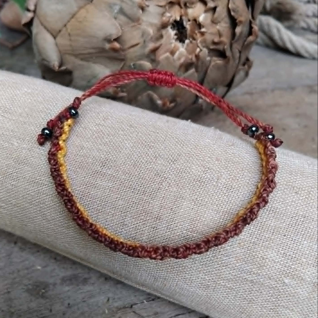 Handcrafted Macrame Knotted bracelet in chocolate brown, saffron yellow and burgundy red cord.  Displayed on a beige linen sleeve.