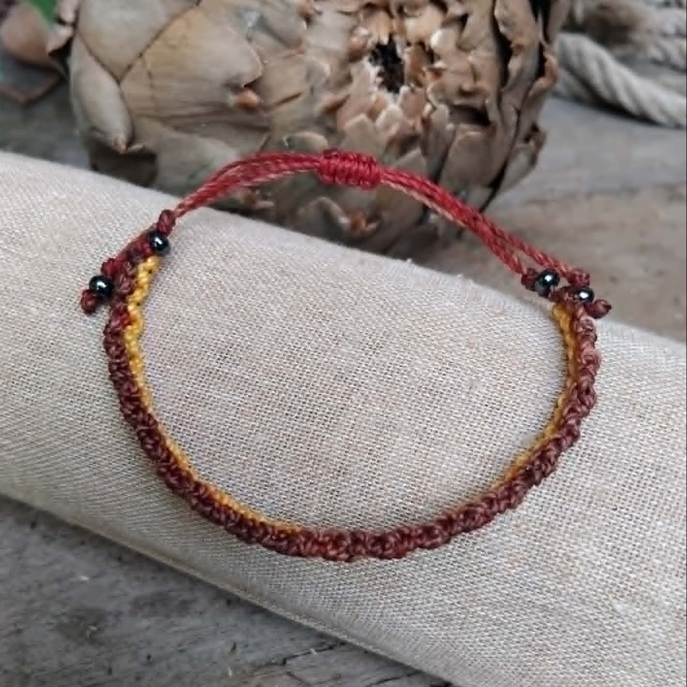 Handcrafted Macrame Knotted bracelet in chocolate brown, saffron yellow and burgundy red cord.  Displayed on a beige linen sleeve.
