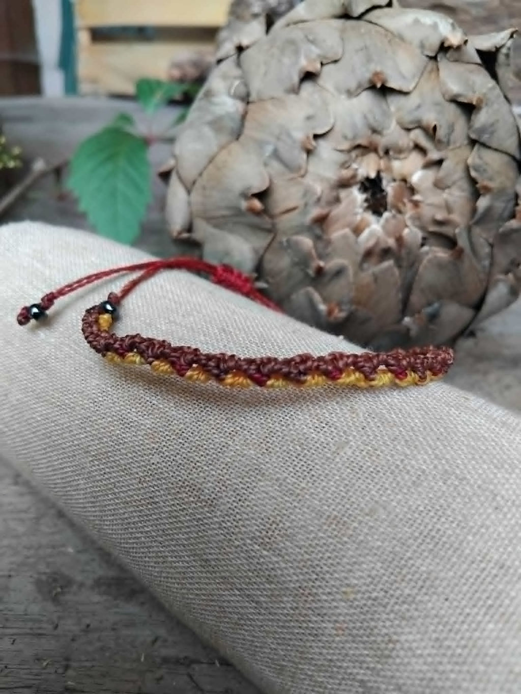Handcrafted Macrame Knotted bracelet in chocolate brown, saffron yellow and burgundy red cord.  Displayed on a beige linen sleeve.