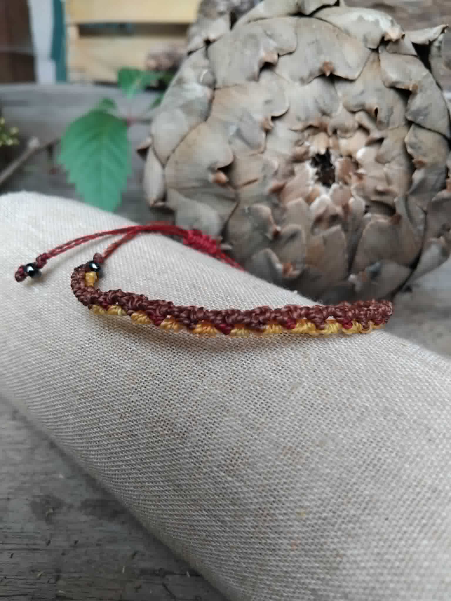 Handcrafted Macrame Knotted bracelet in chocolate brown, saffron yellow and burgundy red cord.  Displayed on a beige linen sleeve.