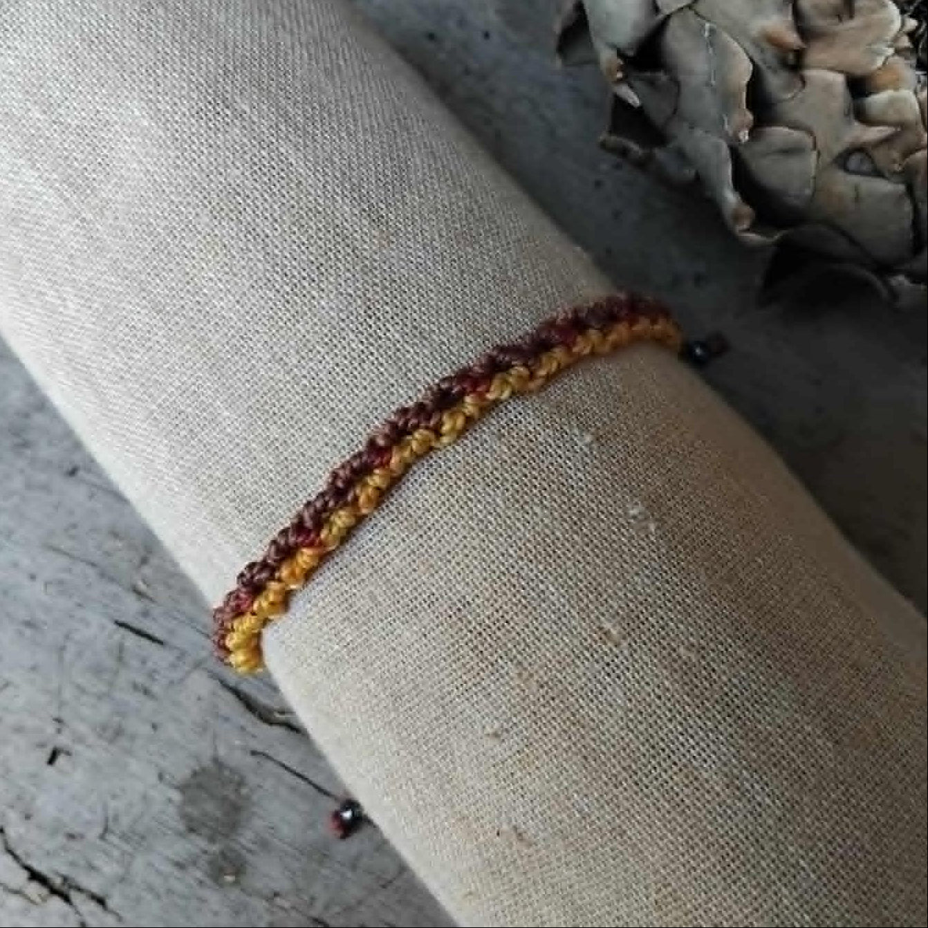 Handcrafted Macrame Knotted bracelet in chocolate brown, saffron yellow and burgundy red cord.  Displayed on a beige linen sleeve.