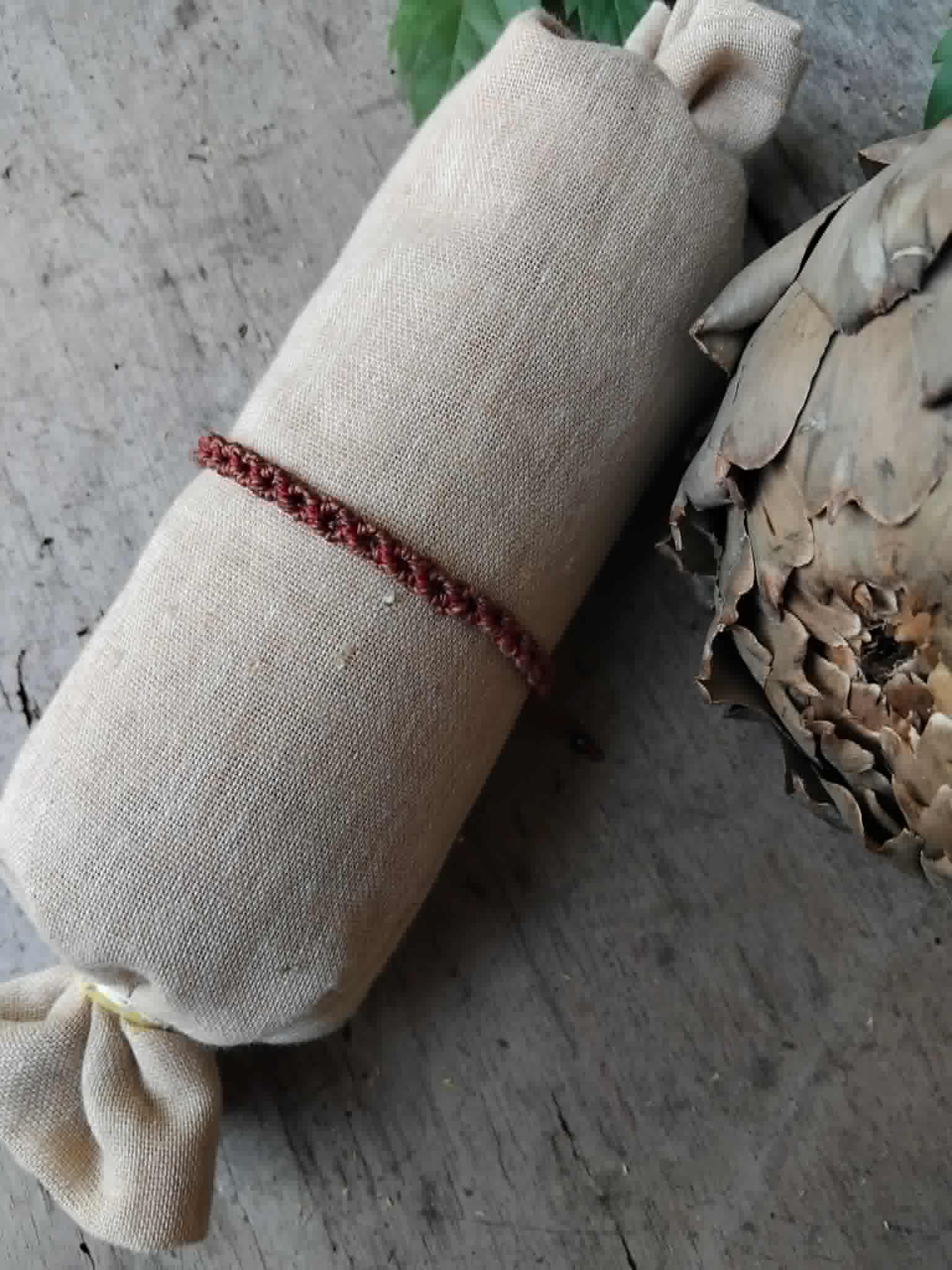 A handcrafted macrame bracelet in chocolate brown cord with burgundy red accents.  Displayed on a beige fabric sleeve, with rustic background.