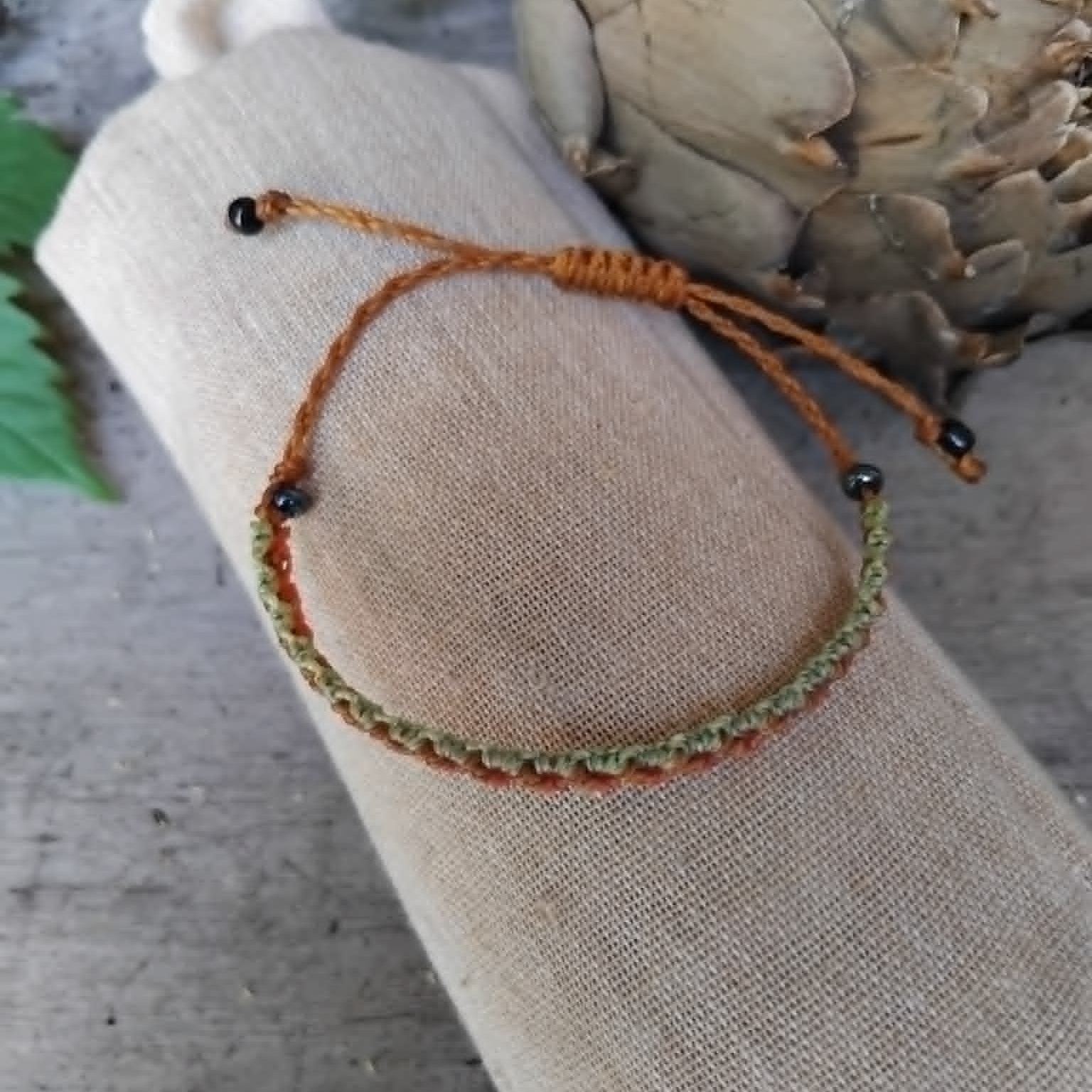 Slim Macrame Bracelet in coral and pale lime green toned waxed cord.  Displayed on a beige linen sleeve.