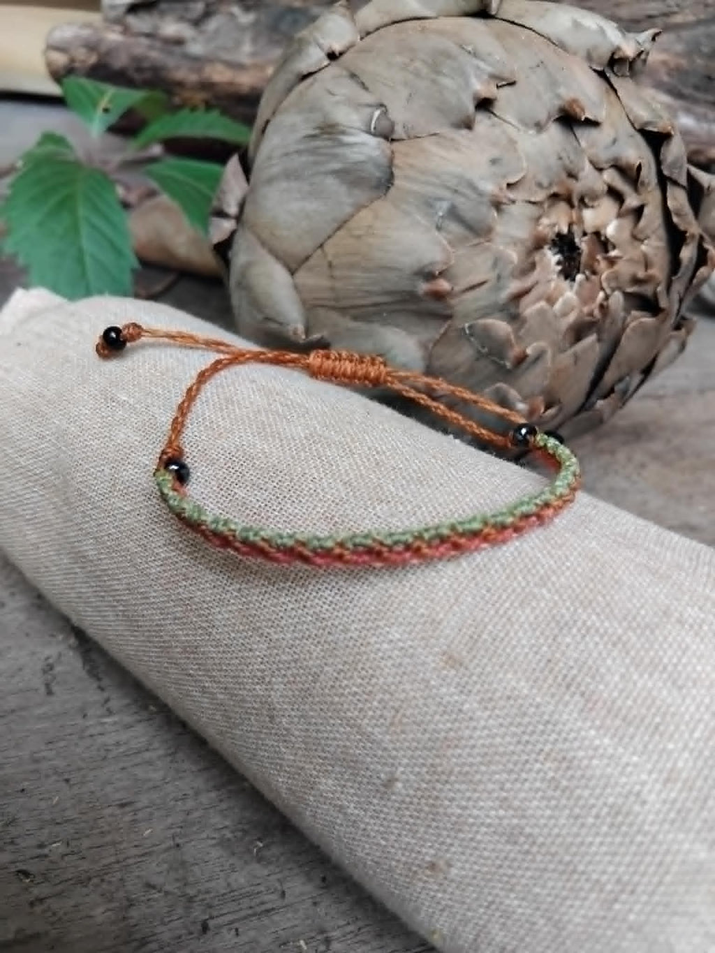 Slim Macrame Bracelet in coral and pale lime green toned waxed cord.  Displayed on a beige linen sleeve.