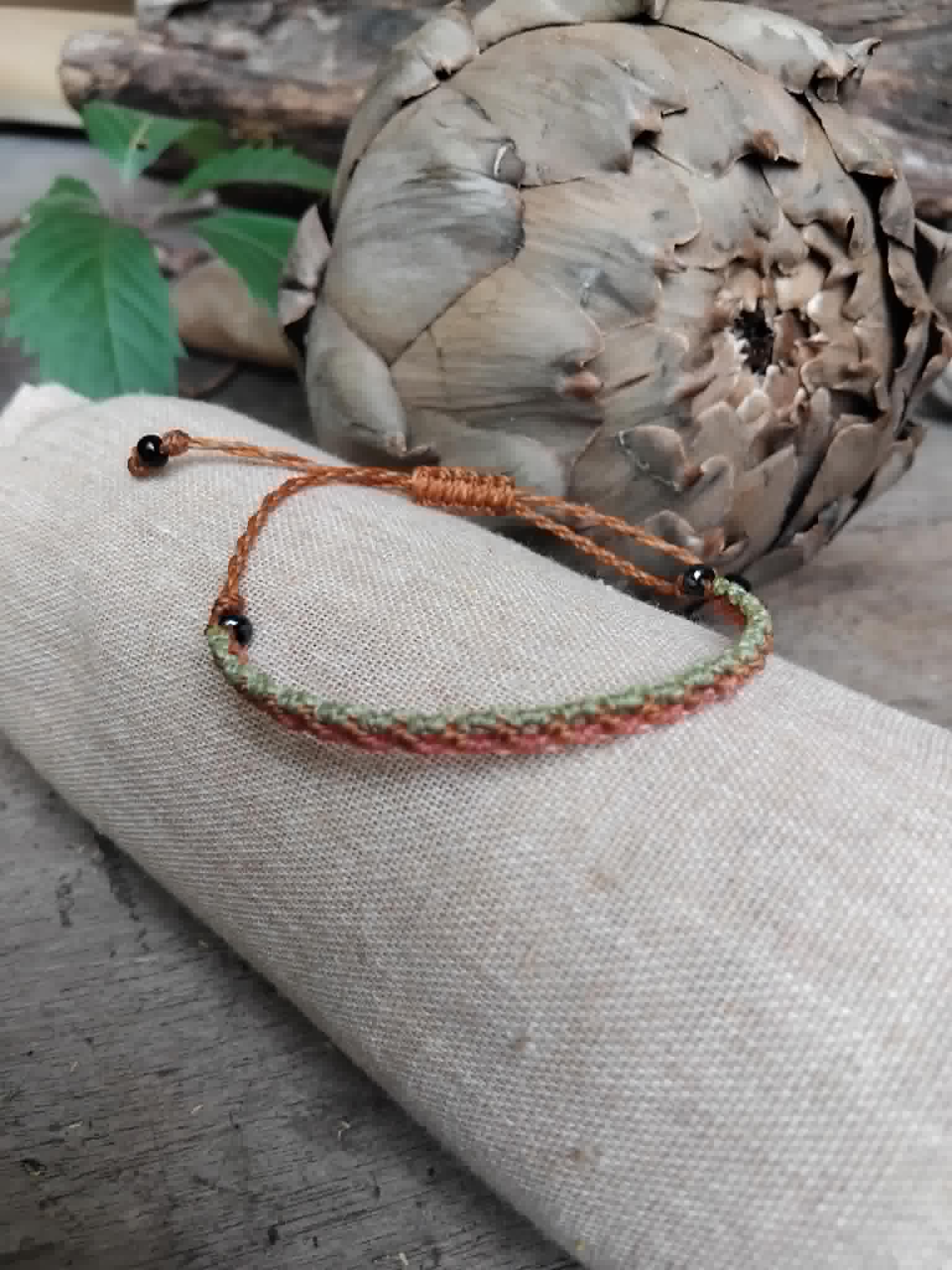 Slim Macrame Bracelet in coral and pale lime green toned waxed cord.  Displayed on a beige linen sleeve.