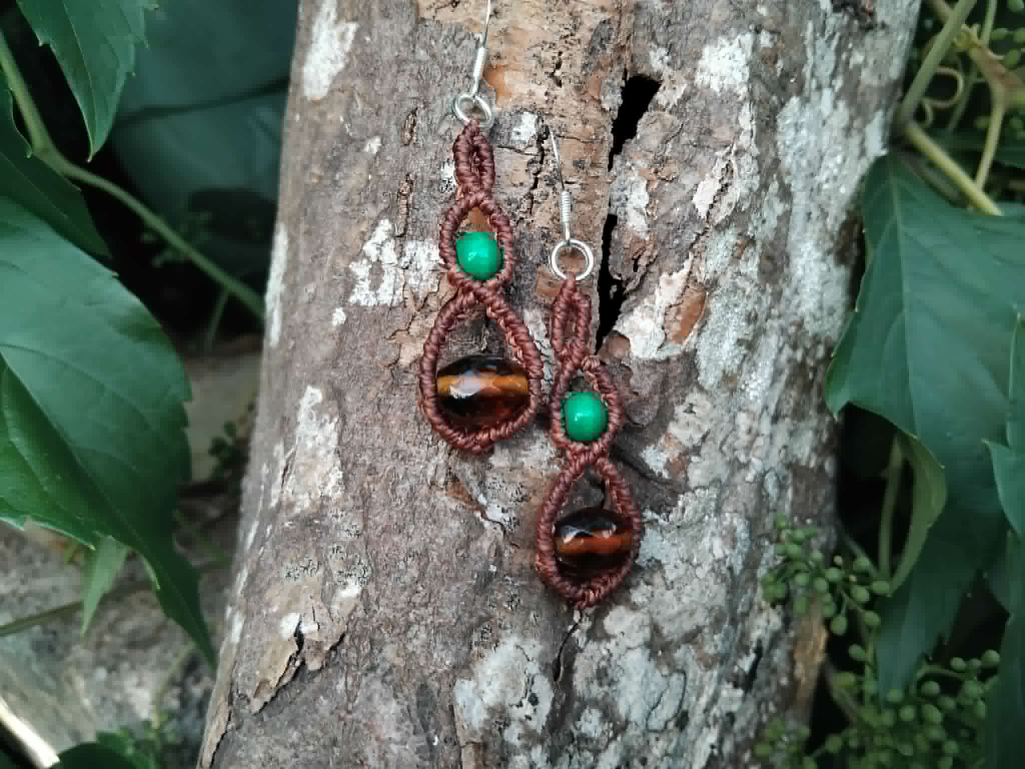 Macrame earrings with silver hooks, wooden green beads and brown glass faceted beads, placed on a piece of tree bark