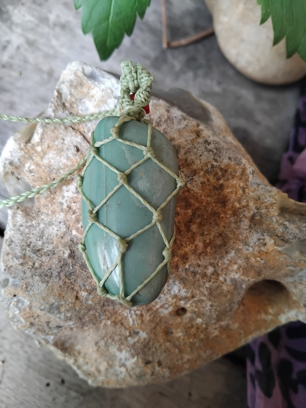Green stone pendant with macrame knotting on a rock