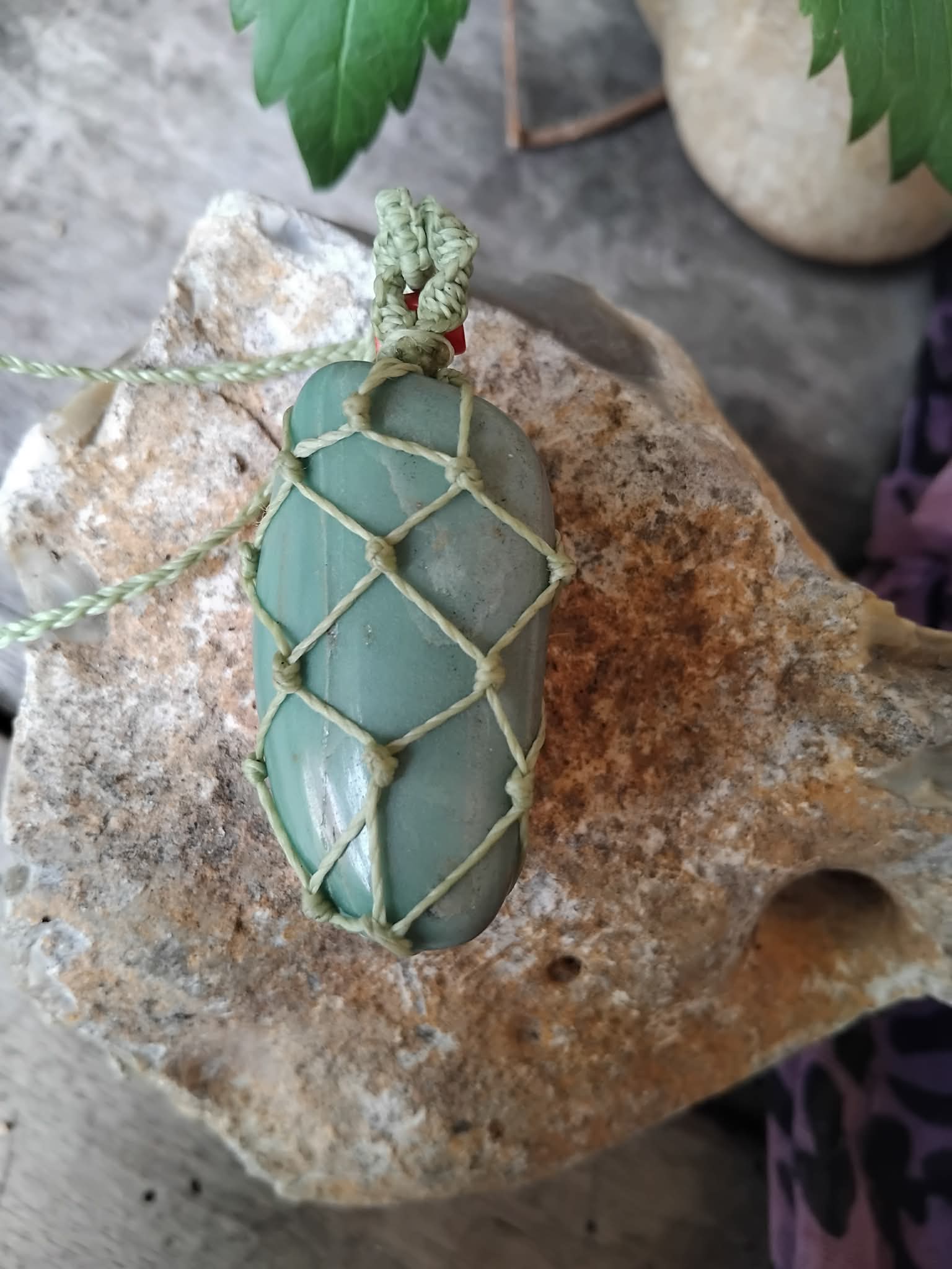 Green stone pendant with macrame knotting on a rock