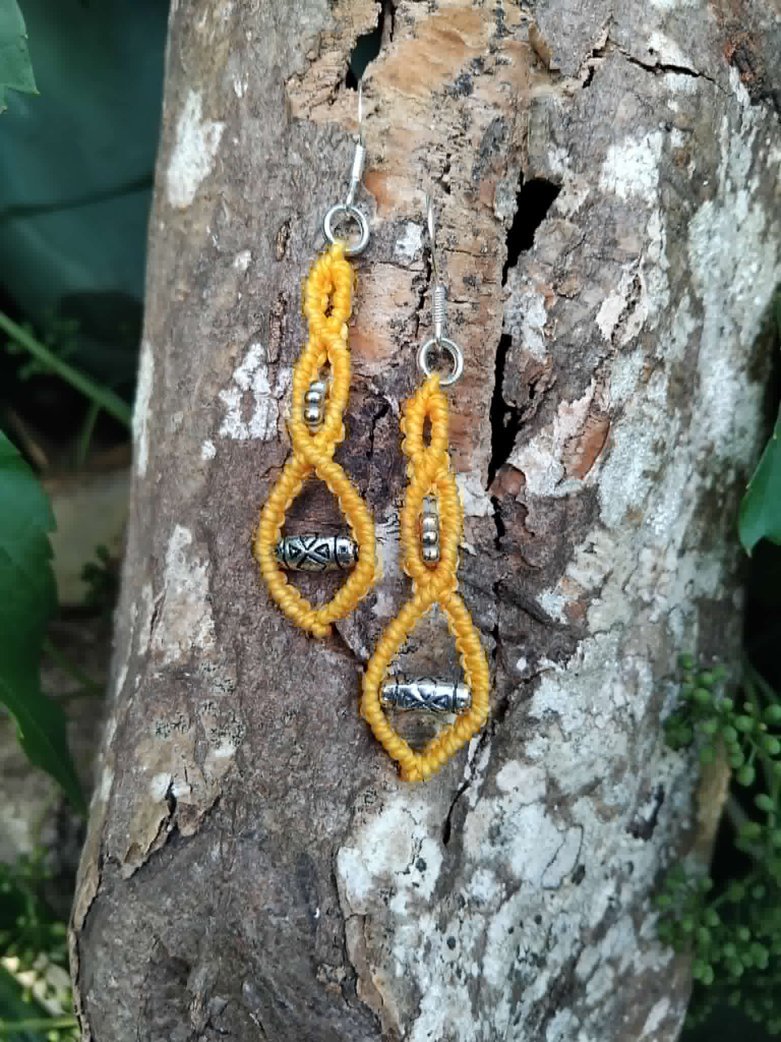 Yellow macrame knotted earrings with silver-toned beads and sterling silver hooks, displayed on a piece of tree bark.