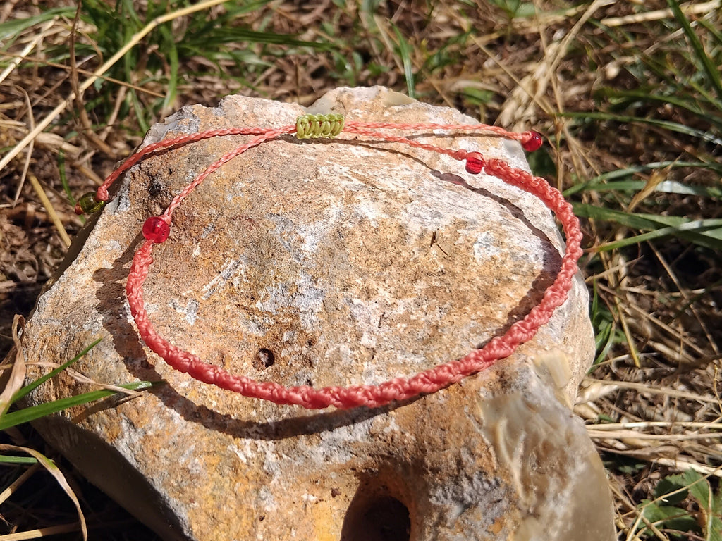 Coral pink macrame bracelet on a stone with grass in the background