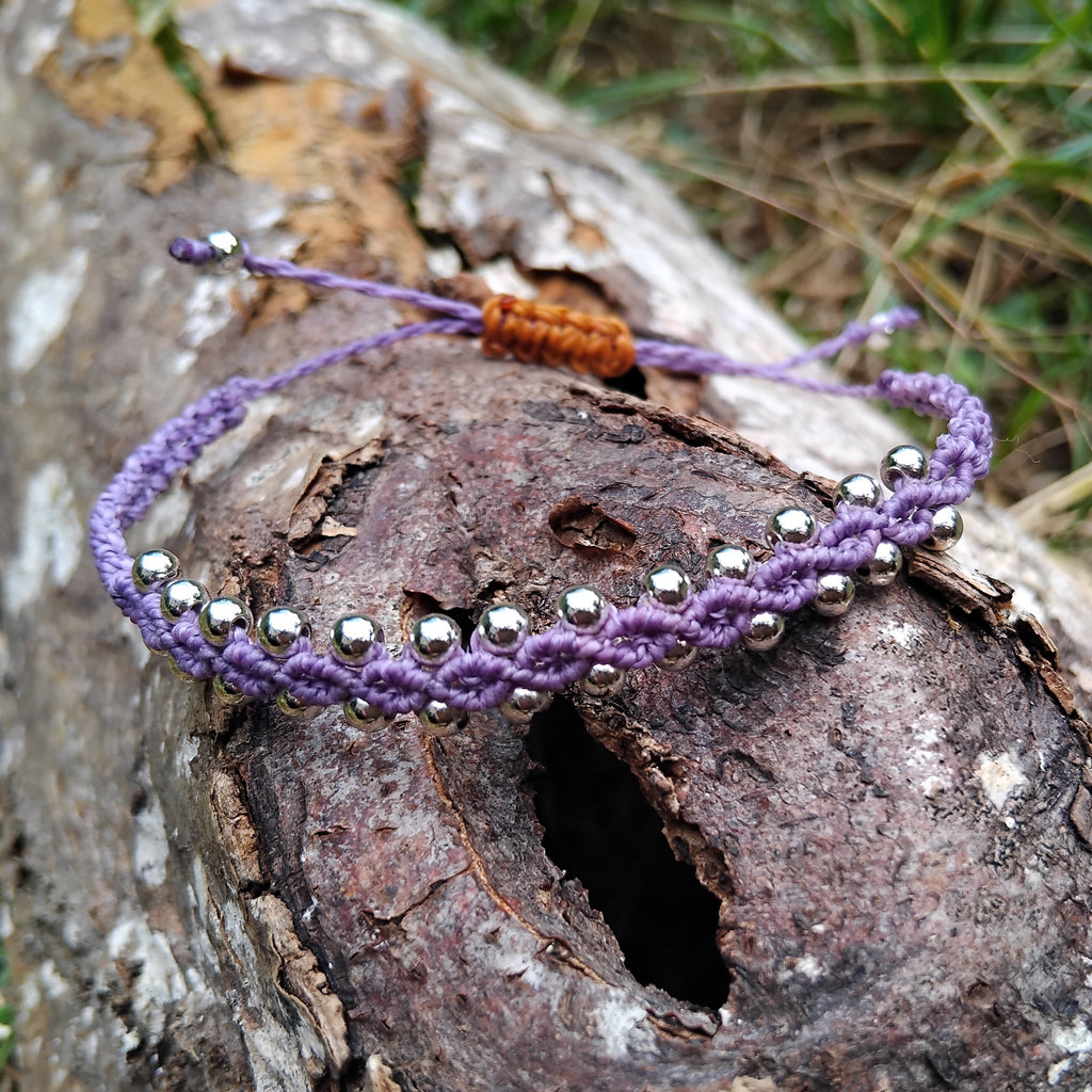 Purple beaded macrame bracelet on a wooden log with grass in the background