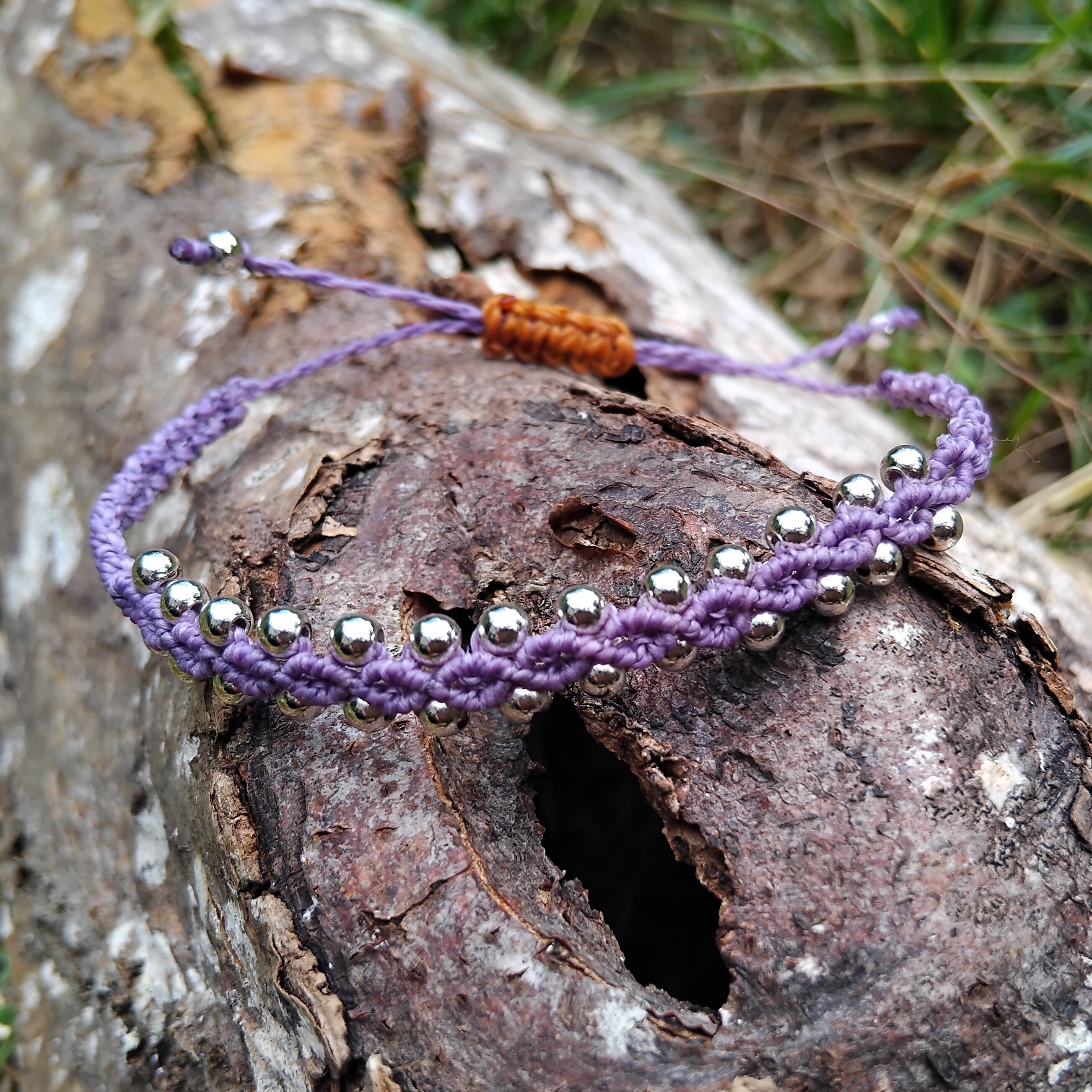 Purple beaded macrame bracelet on a wooden log with grass in the background