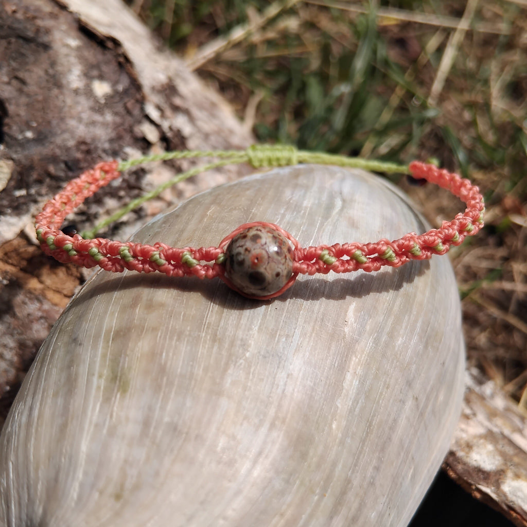 Coral and apple green toned macrame bracelet with a jasper stone effect bead on a shell outdoors