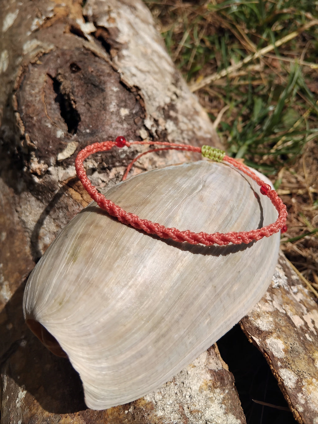 Coral toned macrame bracelet on a large shell with a natural background