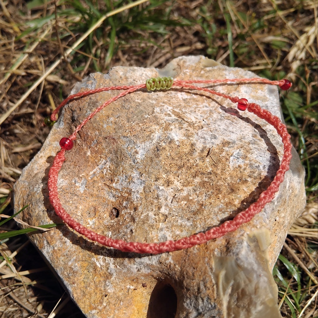 Coral-toned macrame bracelet with beads on a stone in a natural setting