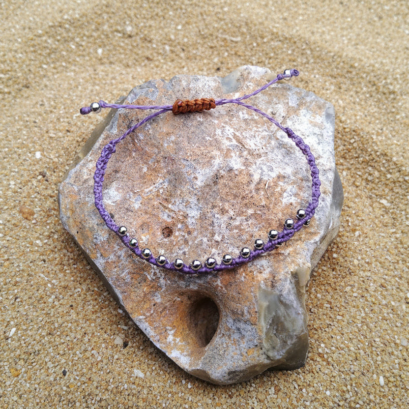 Purple macrame knotted beaded bracelet on a stone with grass in the background