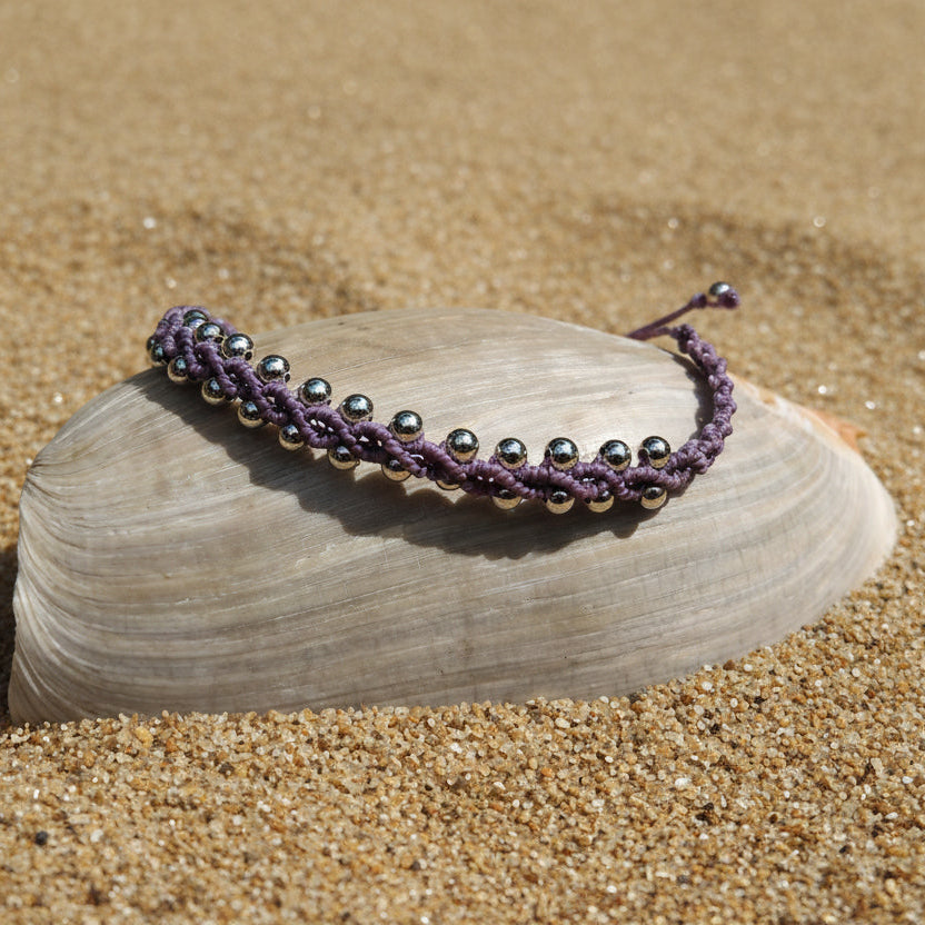 Bracelet with purple waxed knotted macrame and silver beads on a shell outdoors