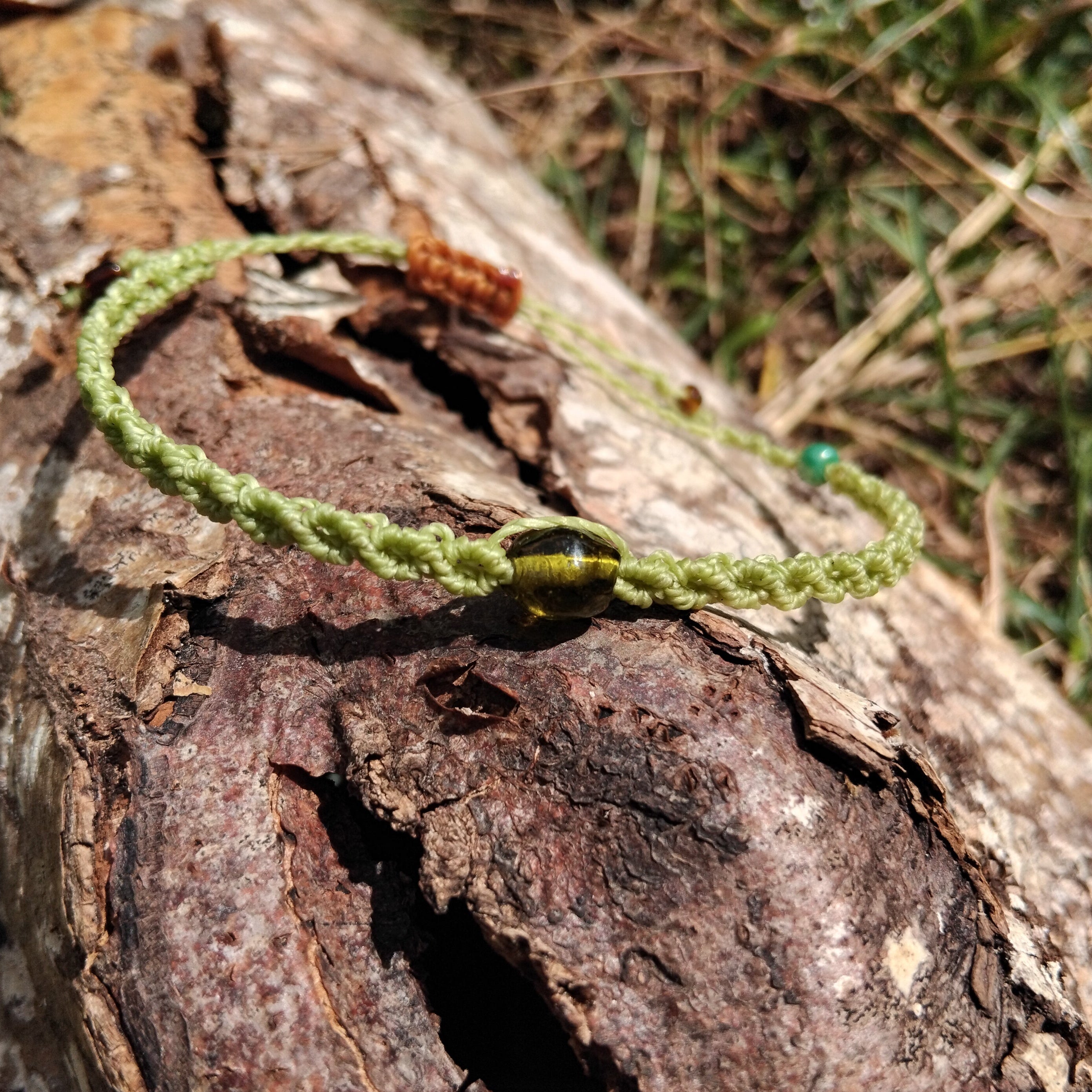 Green macrame bracelet on a textured wooden surface with grass in the background