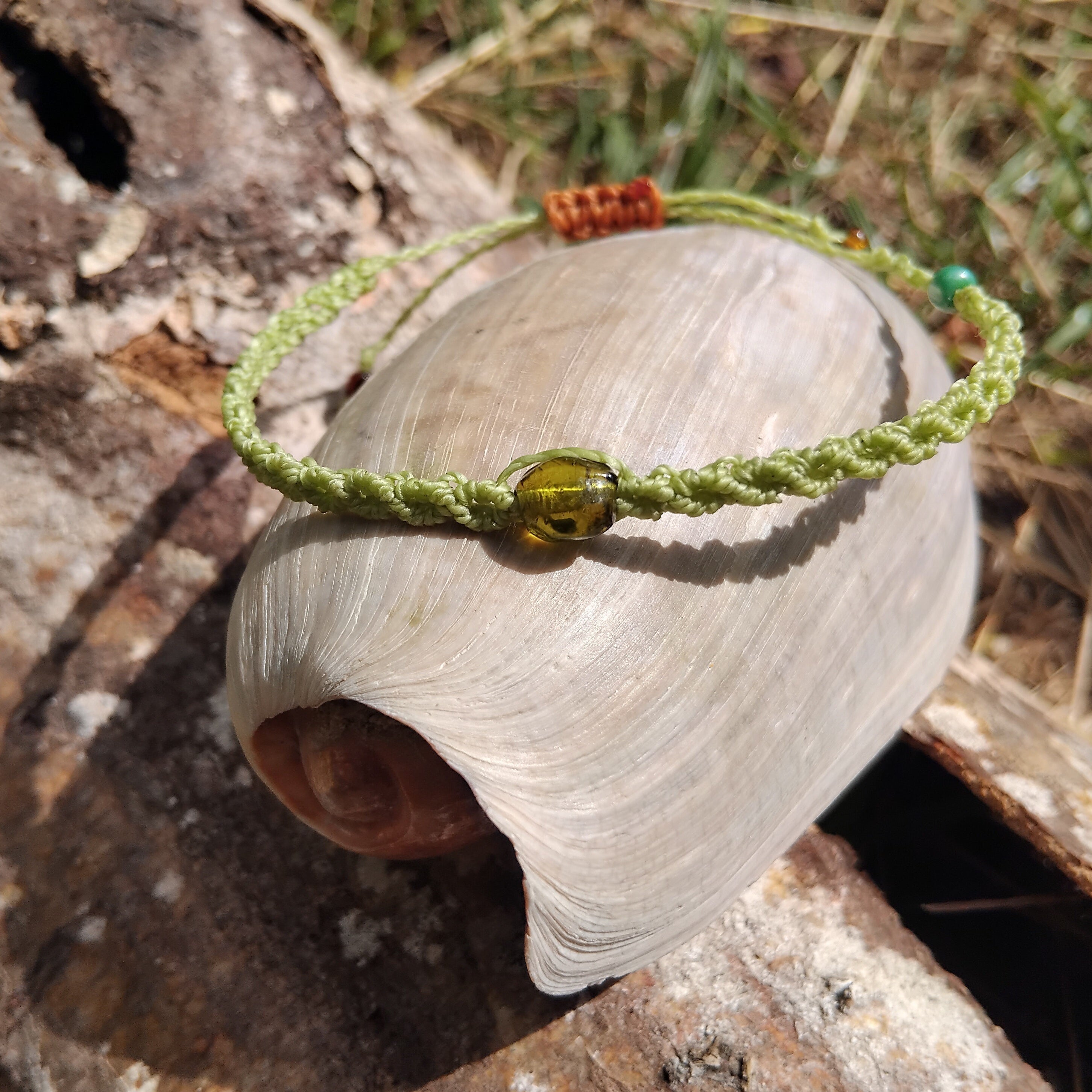 Green macrame bracelet with a green glass bead on a shell against a natural background